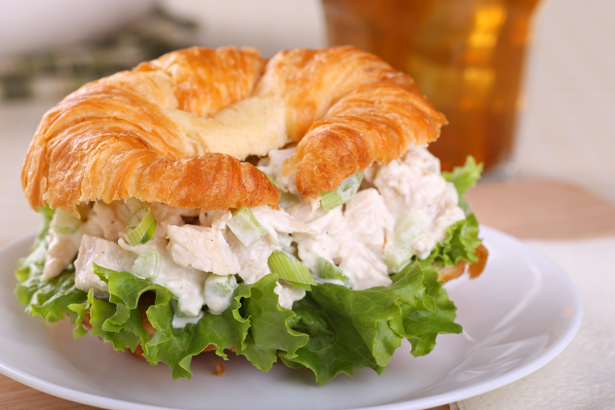 Chicken salad croissant sandwich on a white porcelain plate, selective focus, on a white tablecloth with a blurred background of a glass of beer