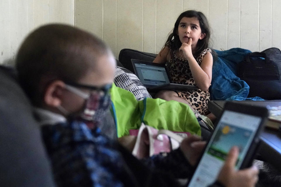 Third grade student Elena thinks while reciting multiplication tables, as her brother Wyatt reviews his kindergarten work on a tablet with their mom, Christi Brouder, in the living room of the family home, while remote learning due to the COVID-19 outbreak, Wednesday, Oct. 14, 2020, in Haverhill, Mass. The Brouder family has four children that are distance learning. Many families with multiple students, some with special needs, are dealing with the challenges of remote distance learning in their home. (AP Photo/Charles Krupa)