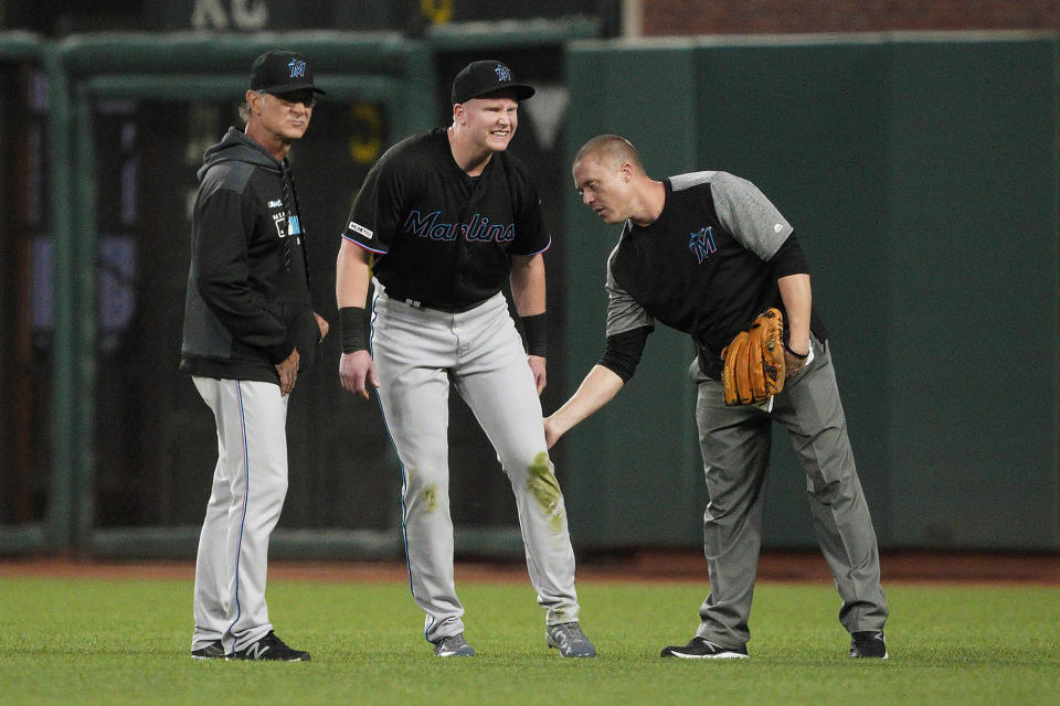 Miami Marlins right fielder Garrett Cooper, center, grimaces as a trainer checks on him and manager Don Mattingly, left, watches during the first inning against the San Francisco Giants in a baseball game Friday, Sept. 13, 2019, in San Francisco. Cooper was taken out of the game. (AP Photo/Tony Avelar)