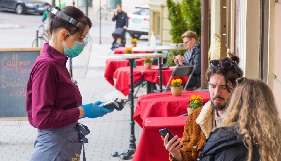 Waitress with a mask and clients at an outdoor bar, cafÃ© or restaurant, reopen after quarantine restrictions.