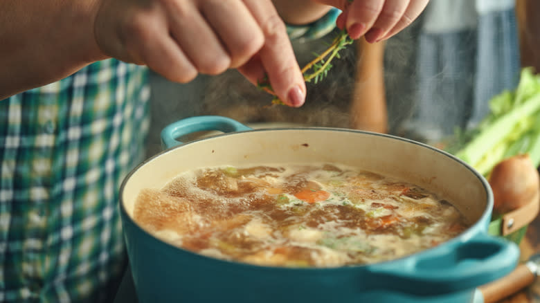 hands placing herbs in soup