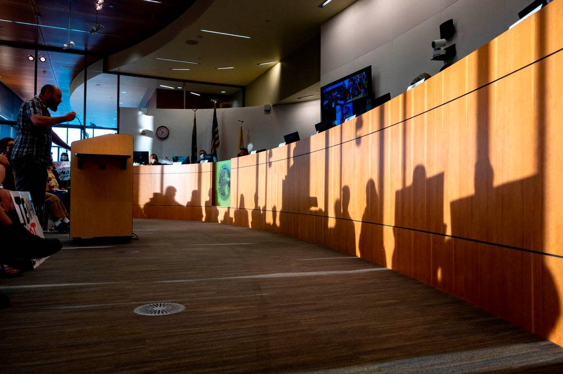 Ty Moore, an organizer with Home in Tacoma For All, addresses the Puyallup City Council as the shadows of several people holding signs are seen in front of him during a meeting on Tuesday, Aug. 23, 2022.