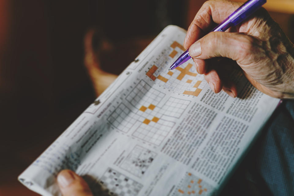 Elderly person's hand completing a crossword puzzle in a newspaper