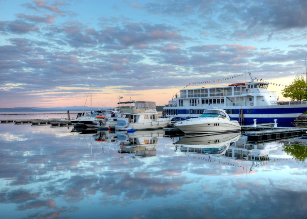 A harbor at sunset; in the foreground, there are several docked boats varying in size and style.