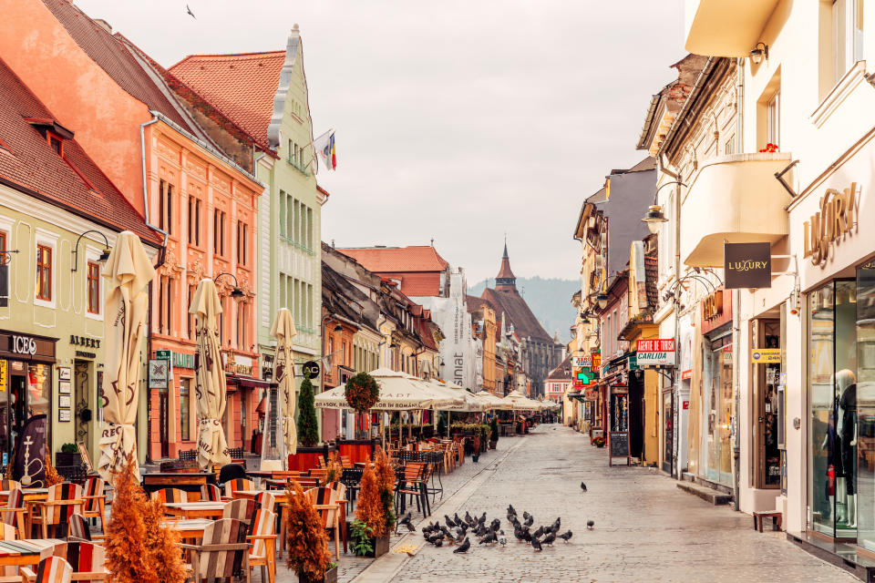 Historic street with buildings, outdoor cafes, and pigeons, no people visible