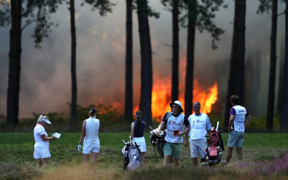 Players, Sophie Powell, Cara Gainer and Gabriella Cowley and their caddies look on as a fire nears the 10th hole during day three of The Rose Ladies Series on The West Course in the first ever ladies professional event at Wentworth Golf Club - GETTY IMAGES