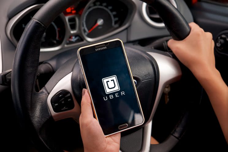 A person uses the Uber app while seated behind the wheel of a car. (Digital Trends)