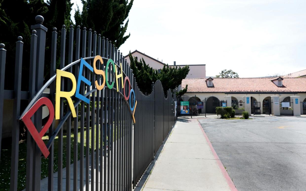 A fenceline, with a sign reading "Preschool," and school buildings