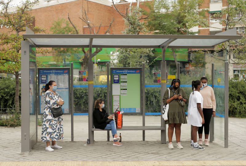 People wearing protective face masks wait at a bus stop at Usera neighbourhood in Madrid