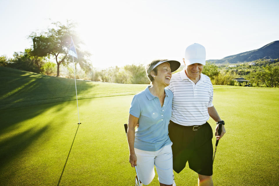 Senior husband and wife couple walking off green on golf course laughing. A new ALS survey found golfing may increase men's risk of developing ALS, but an expert says it doesn't have to mean you have to quit.  (Image via Getty Images)