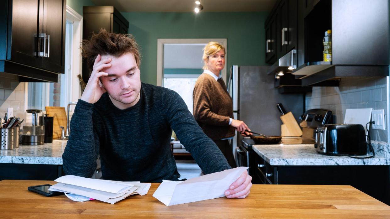 A young man sitting at home stressed by his mounting debts.