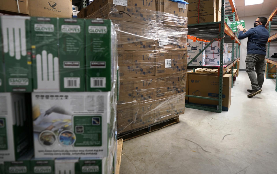 Ray Bellia stocks shelves with personal protective gloves, used by medical and law enforcement professionals, while unpacking pallets of other PPE goods in the warehouse of his Body Armor Outlet store, Wednesday, Dec. 9, 2020, in Salem, N.H. A nationwide analysis of state purchasing data by The Associated Press showed governors' administrations spent at least $7 billion to purchase personal protective equipment and high-demand medical devices during the first frenzied months of the coronavirus pandemic. Bellia adapted his inventory and supply chain as the pandemic hit toward delivering PPE goods, which were a minor part of his business in previous years. (AP Photo/Charles Krupa)