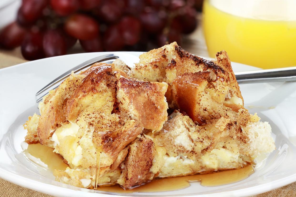 French toast casserole with maple syrup. Made with cream cheese cheese in the center. Fresh grapes and orange juice in background.