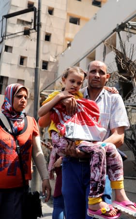 An Egyptian man carries his daughter with cancer as he walks in front of the damaged facade of the National Cancer Institute after an overnight fire from a blast, in Cairo