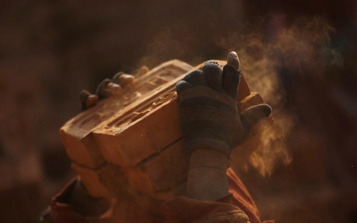 Dust blows as a worker stacks bricks on his head at a brick factory - REUTERS
