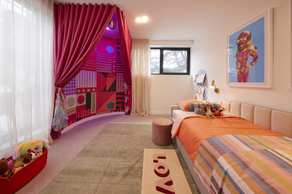 A wide shot of the room with a curved wall with patterns and a pink curtain in front of it. A day bed to the right and a rug that reads 'love' in front of it.