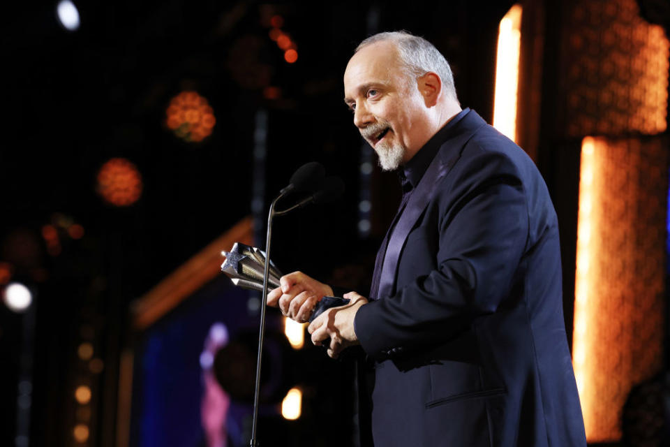 Paul in suit holding award at a podium with stage background