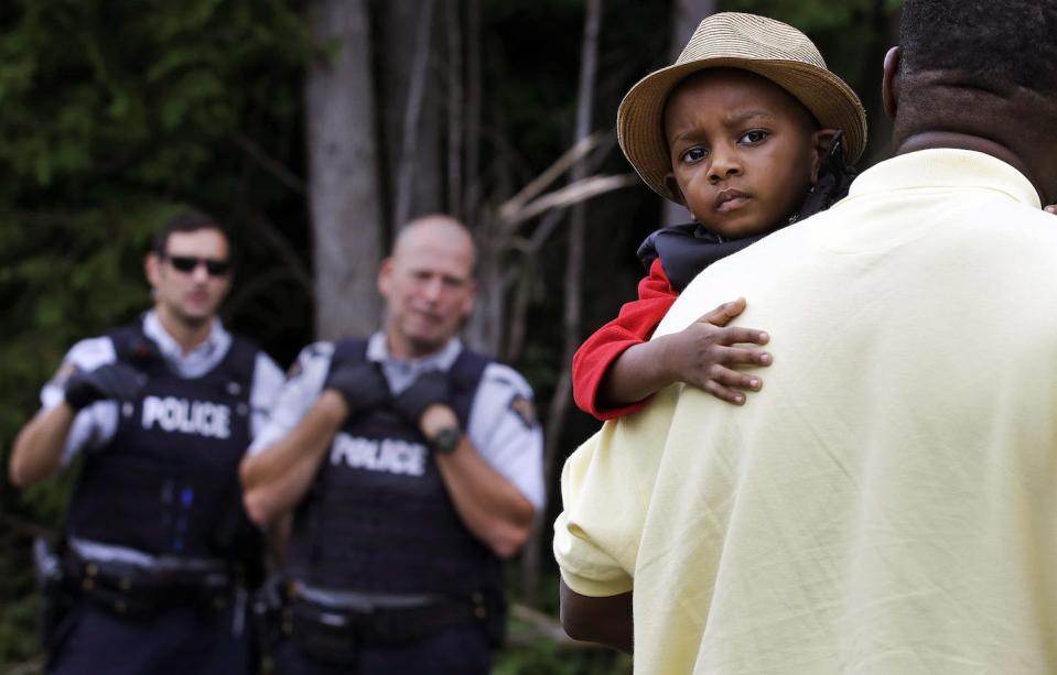 A Haitian boy holds onto his father as they approach an irregular border crossing staffed by the RCMP, near Saint-Bernard-de-Lacolle, Québec, in 2017. (AP Photo/Charles Krupa)