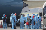 Vietnamese COVID-19 patients in protective gear, holding Vietnamese flags and carrying a portrait of the national leader Ho Chi Minh, arrive at the Noi Bai airport in Hanoi, Vietnam, on Wednesday, July 29, 2020. The 129 patients who were working in Equatorial Guinea are brought home in a repatriation flight for treatment of the coronavirus. (Tran Huy Hung/VNA via AP)