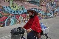 A traditional herbal drink vendor wearing a mask to help curb the spread of the coronavirus outbreak cycles past a mural with writings that read "Jakarta gives without expecting anything in return," in Jakarta, Indonesia, Tuesday, Aug. 4, 2020. (AP Photo/Dita Alangkara)