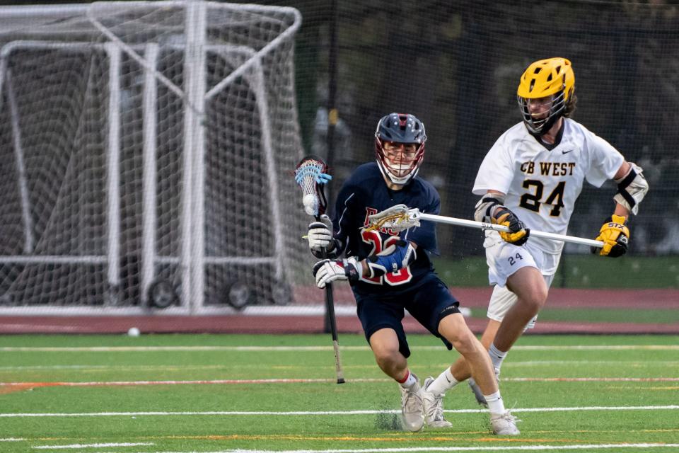 Central Bucks East's Aiden Schmidt cradles the ball while covered by Central Bucks West's Cameron Wassmann in a boys lacrosse game at Central Bucks West High School in Doylestown, on Tuesday, April 26, 2022. The Patriots defeated the Bucks 13-7.