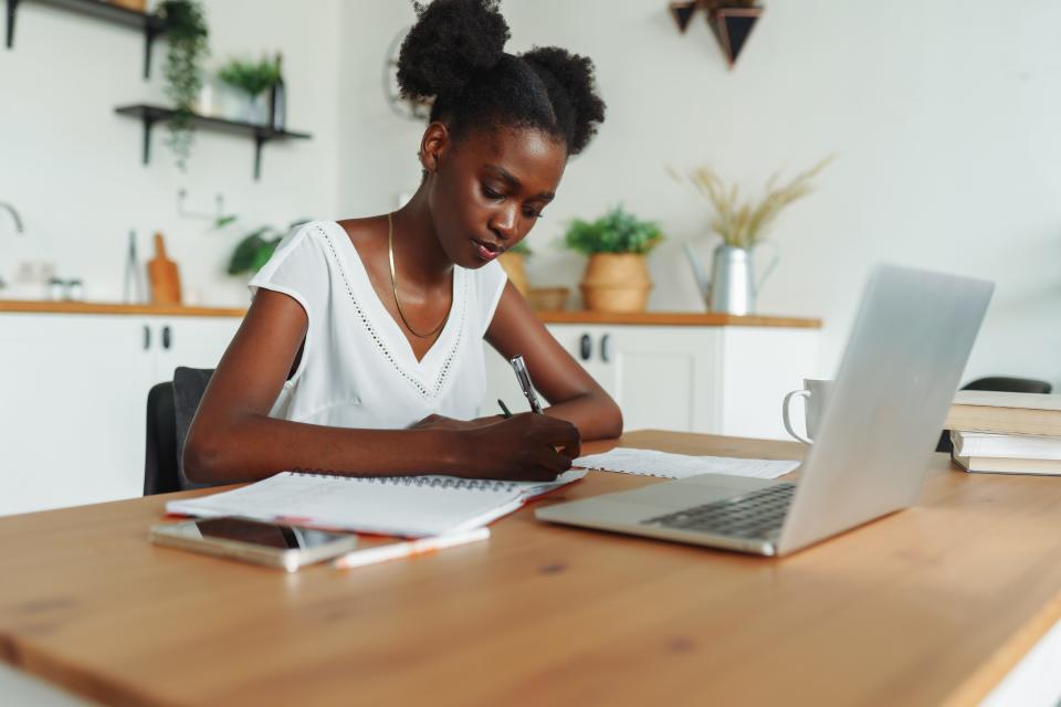 A woman sitting at a desk with a laptop and stationary writing on a piece of paper.