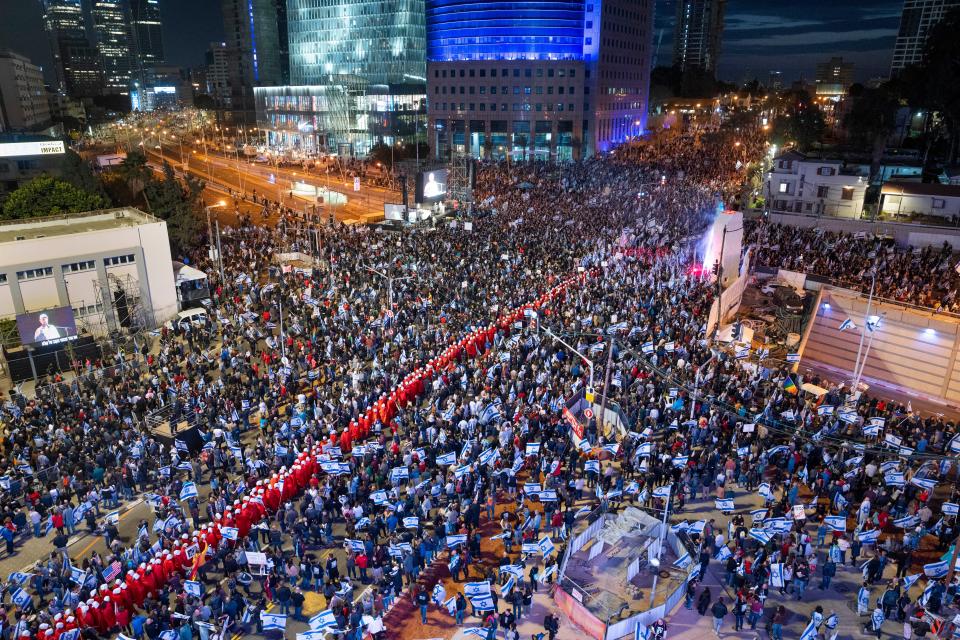 A line of protesters supporting women's rights dressed as characters from The Handmaid's Tale television series and other Israelis protest against plans by Prime Minister Benjamin Netanyahu's government to overhaul the judicial system in Tel Aviv, Israel, Saturday, March 25, 2023.