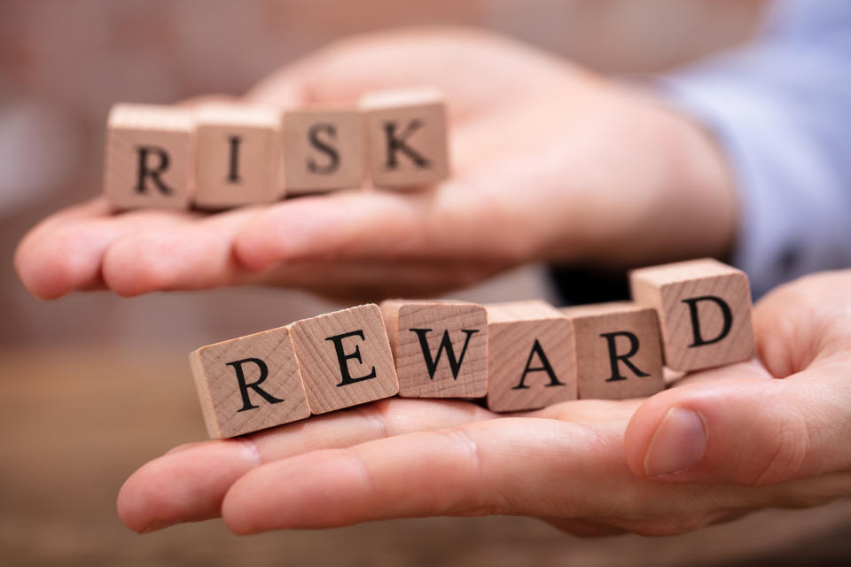 Hands holding blocks that spell out 'risk' and 'reward.'