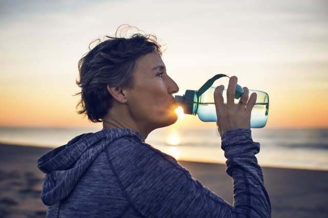 Close-up of woman drinking water at beach against sky