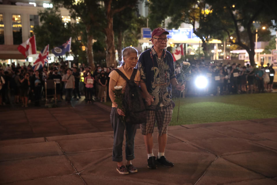 A couple with flowers stand in silence in front of the Cenotaph as they gather to celebrate the 74th Anniversary of the Liberation of Hong Kong, Friday, Aug. 30, 2019, in Hong Kong. Police have appealed to Hong Kong residents to stay from any non-authorized rallies on Saturday after authorities banned a major march, warning that those caught could face a five-year jail term. (AP Photo/Jae C. Hong)