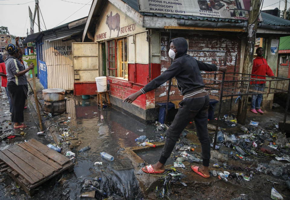 A boy wears a mask as a preventative measure against the spread of the new coronavirus, as he navigates a flood of water mixed with garbage following heavy rains, in the Kibera slum, or informal settlement, of Nairobi, Kenya, Thursday, March 26, 2020. Many slum residents say staying at home or social-distancing is impossible for those who live hand to mouth and receive daily wages for informal work, as is maintaining sanitation in densely populated areas where a pit latrine can be shared by over 50 people. (AP Photo/Brian Inganga)