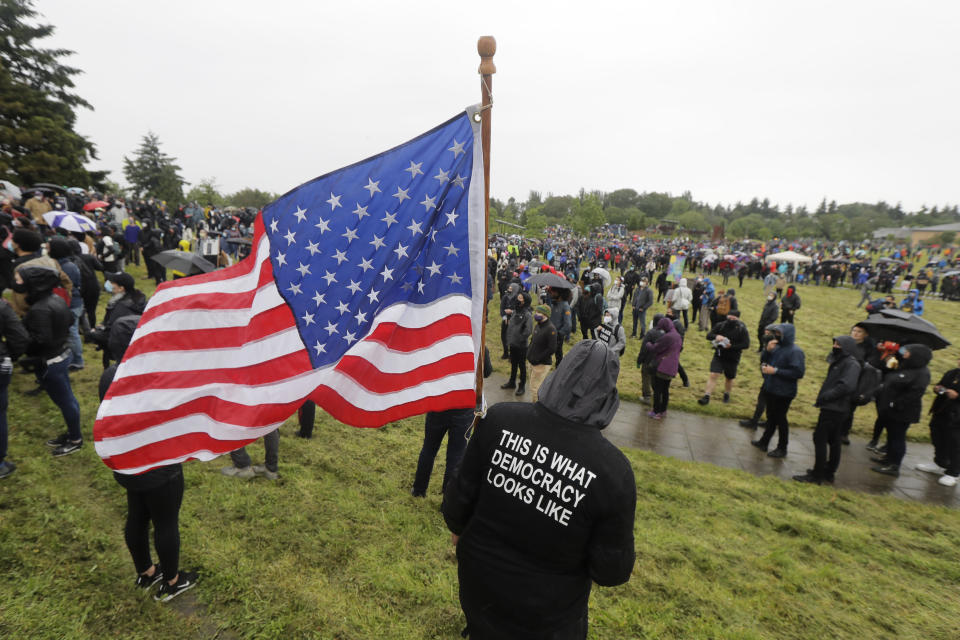 A protester holds a United States flag while wearing a jacket that reads "This is What Democracy Looks Like" during a rally that followed a "Silent March" against racial inequality and police brutality that was organized by Black Lives Matter Seattle-King County, Friday, June 12, 2020, in Seattle. Hundreds of people marched for nearly two miles to support Black lives, oppose racism and to call for police reforms among other issues. (AP Photo/Ted S. Warren)