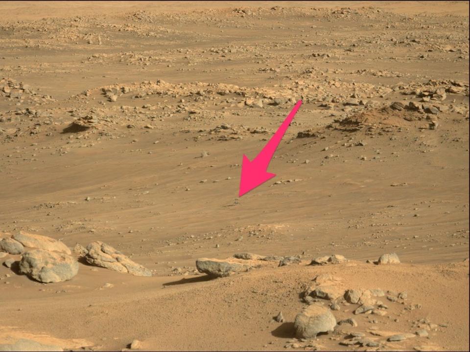 orange brown dusty rocky mars landscape with ingenuity helicopter tiny in the distance