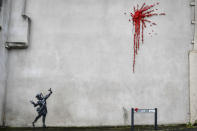 A woman walks past a new artwork on the side of a house in Bristol, England, Thursday Feb. 13, 2020, which has been confirmed as the work of street artist Banksy. (Ben Birchall/PA via AP)