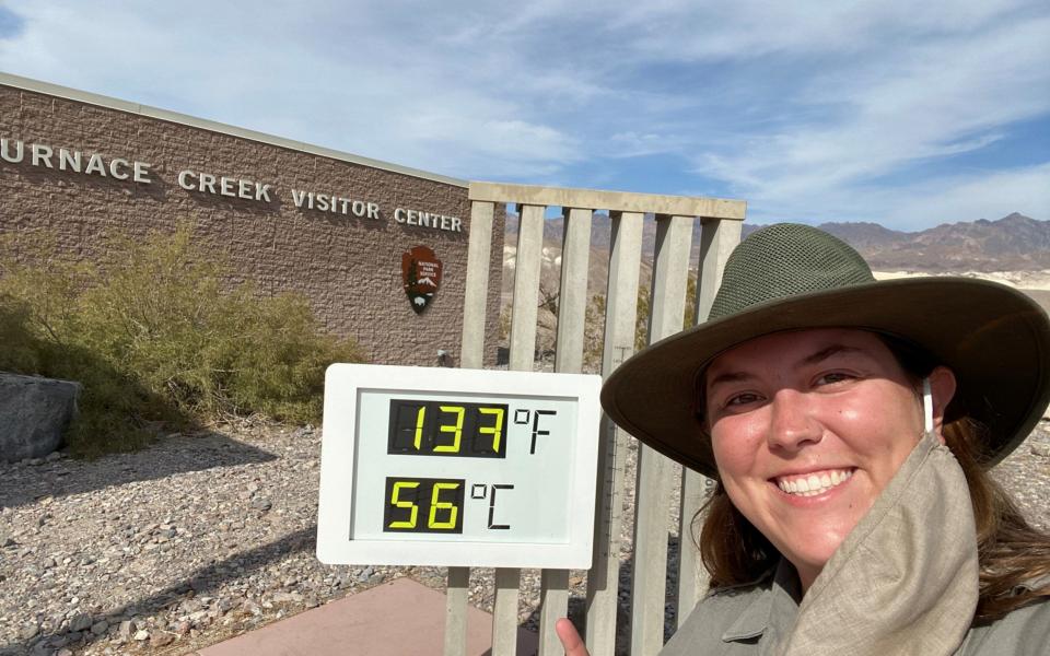 An employee of Death Valley National Park poses next to an sign showing the potentially record-breaking temperature - CAROLINE ROHE
