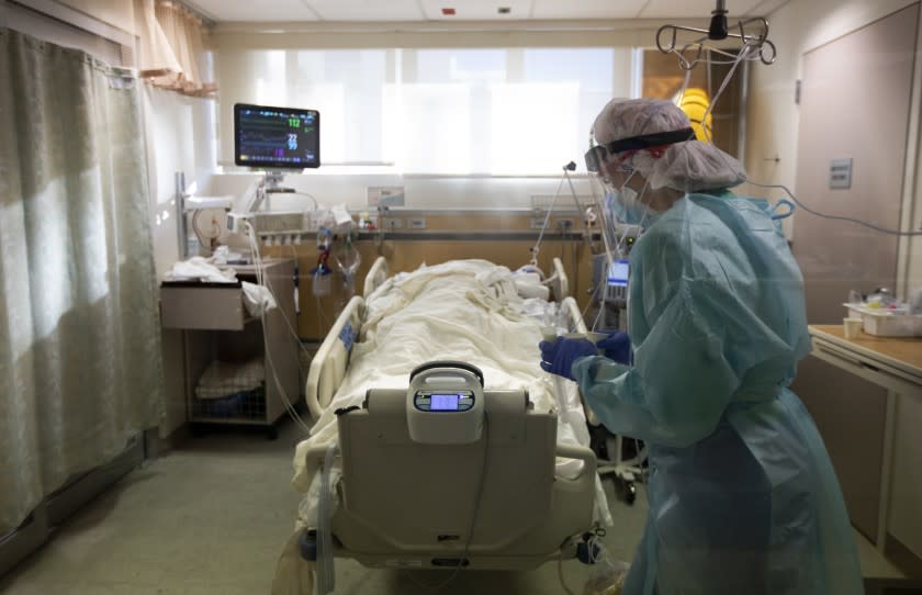 FULLERTON, CA - DECEMBER 25: Bringing in medication Registered Nurse Joan Pung, weaves her way through IV lines in a covid positive patients room inside the ICU at Providence St. Jude Medical Center Christmas Day on Friday, Dec. 25, 2020 in Fullerton, CA. The IV stands have been placed outside the rooms of the covid patients to help the nurses from constantly going into the rooms for their safety from exposure to the virus. The nurses are careful to maneuver through the lines. (Francine Orr / Los Angeles Times)