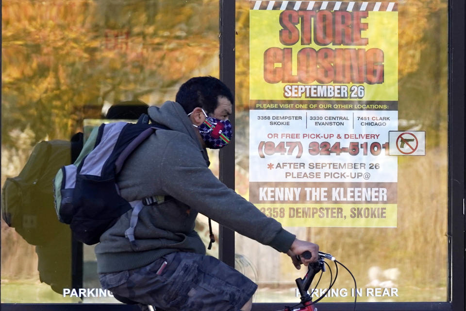 FILE - In this Friday, Nov. 6, 2020, file photo, a man wearing a face mask rides a bicycle past a closed store in Wilmette, Ill. States in the U.S. are renewing their push for more federal money to deal with the fallout from the coronavirus outbreak and to help them distribute a vaccine when one becomes widely available sometime in 2021. (AP Photo/Nam Y. Huh, File)