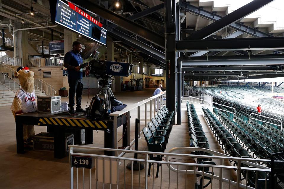 <p>Blooper, mascot of the Atlanta Braves, watches a television cameraman during the exhibition game between the Atlanta Braves and the Miami Marlins at Truist Park.</p>