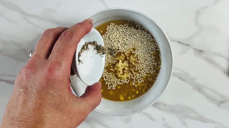 hand adding seasonings to bowl of sauce