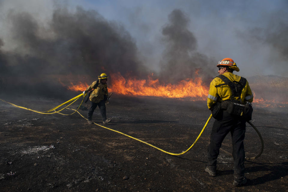 Firefighters work to prevent flames from reaching nearby homes while battling the Easy Fire, Wednesday, Oct. 30, 2019, in Simi Valley, Calif. It has chewed through brush and trees near suburbs, horse ranches and the Ronald Reagan Presidential Library. (AP Photo/Christian Monterrosa)