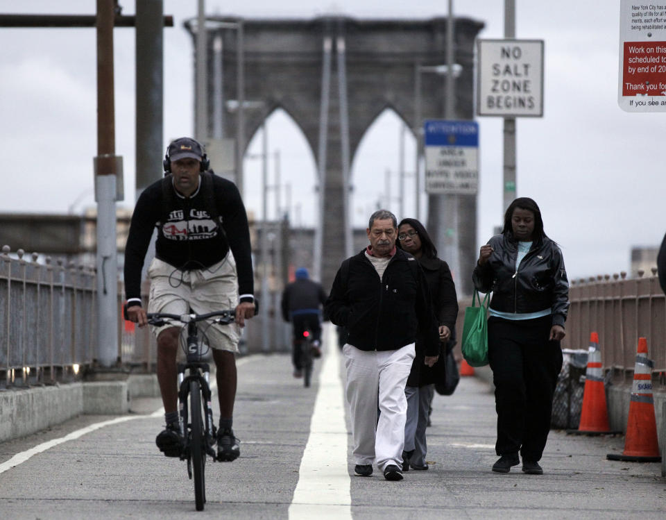 FILE - In this Oct. 31, 2012 file photo, morning commuters walk and bicycle across New York's Brooklyn Bridge. On the Brooklyn Bridge, closed earlier because of high winds, joggers and bikers made their way across the span before sunrise. Car traffic on the bridge was busy, and slowed as it neared Manhattan. Nearly every office dweller fantasizes about the joys of working from home, but Superstorm Sandy has created legions of people who can't wait to get back to the office. (AP Photo/Richard Drew, File)