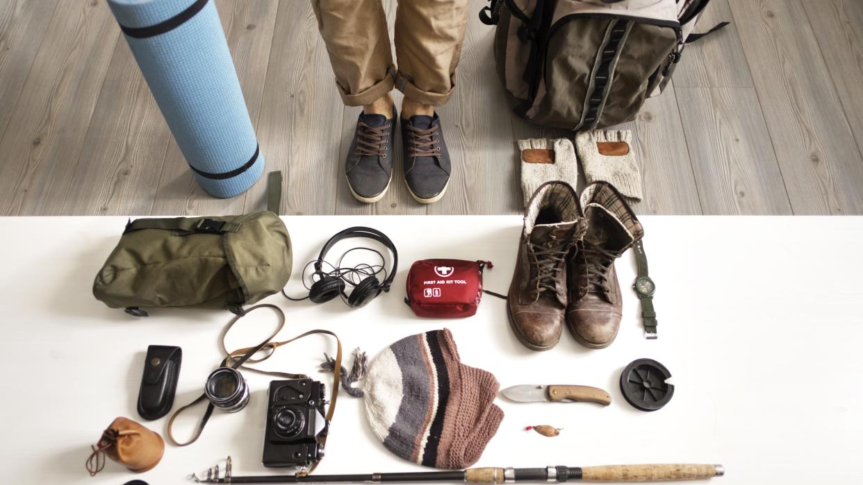  Low section of man standing with hiking and fishing gear arranged on table at home. 