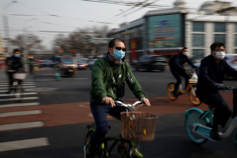 People wearing face masks ride bicycles on a street following an outbreak of the coronavirus disease (COVID-19), in Beijing, China