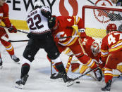 Arizona Coyotes forward Jack McBain (22) battles for the puck with Calgary Flames defenseman Rasmus Andersson (4) as goalie Dustin Wolf (32) tries to grab it during the first period of an NHL hockey game in Calgary, Alberta, Sunday, April 14, 2024. (Jeff McIntosh/The Canadian Press via AP)