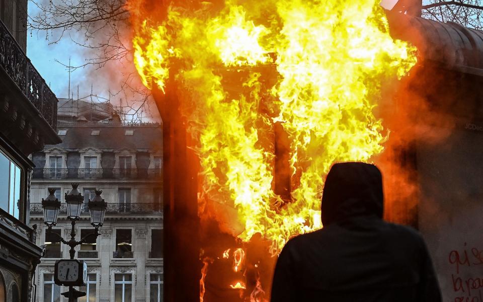 A protester wearing a hood stands next to a burning new kiosk beside the Place de l'Opera - ALAIN JOCARD