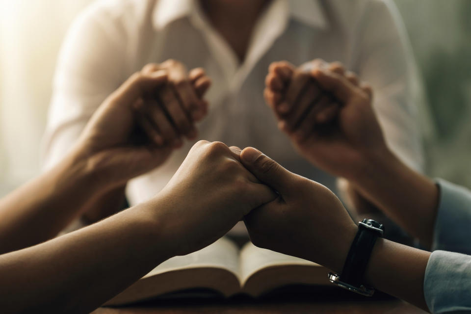 People holding hands over an open book in a prayer circle