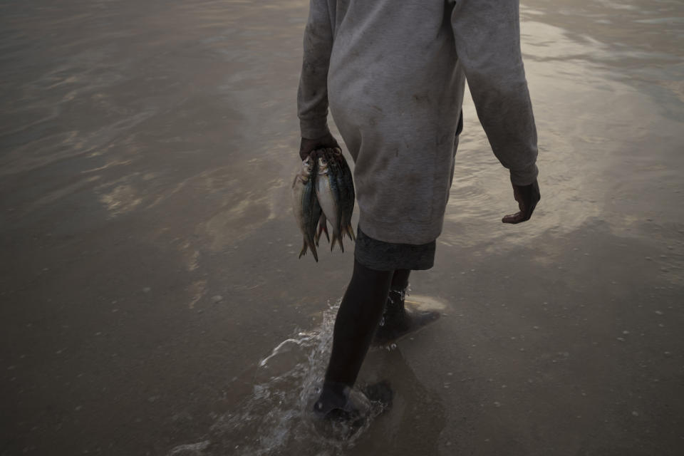 A man holds fish as he walks on the beach in Nouakchott, Mauritania, Friday, Dec. 10, 2021. (AP Photo/Felipe Dana)