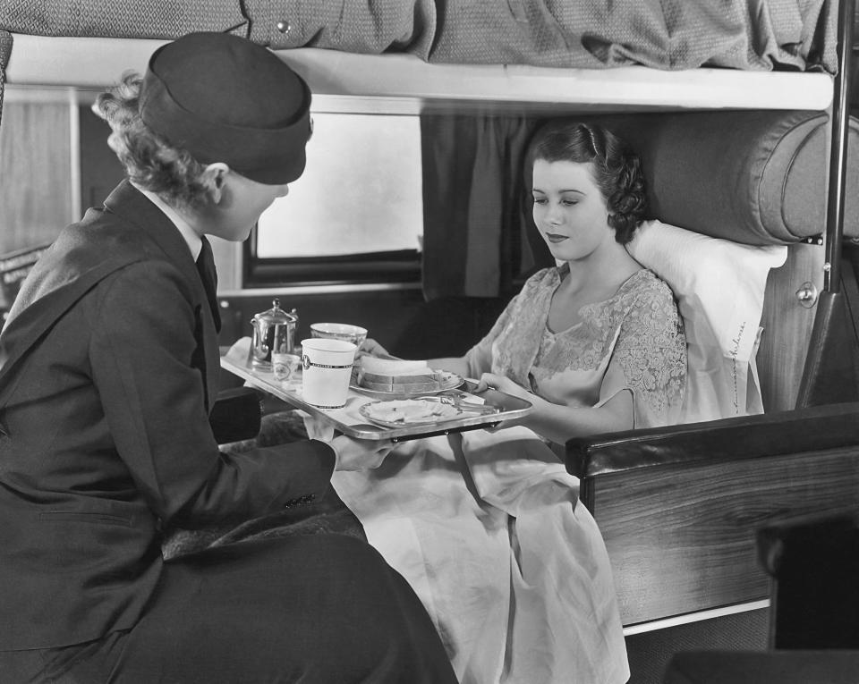 A flight attendant serves coffee and sandwiches to a passenger on board an American Airlines flight, circa 1935.&nbsp;