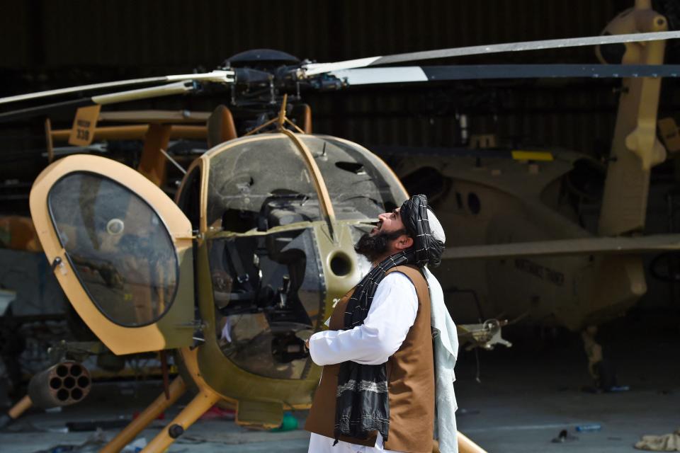 A Taliban member looks up standing next to a damaged helicopter at the airport in Kabul on August 31, 2021, after the US has pulled all its troops out of the country to end a brutal 20-year war -- one that started and ended with the hardline Islamist in power. (Photo by Wakil KOHSAR / AFP) (Photo by WAKIL KOHSAR/AFP via Getty Images)