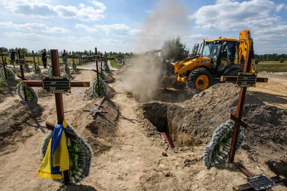 An excavator covers coffins containing one of 15 unidentified people killed by Russian forces amid Russia's ongoing assault on Ukraine